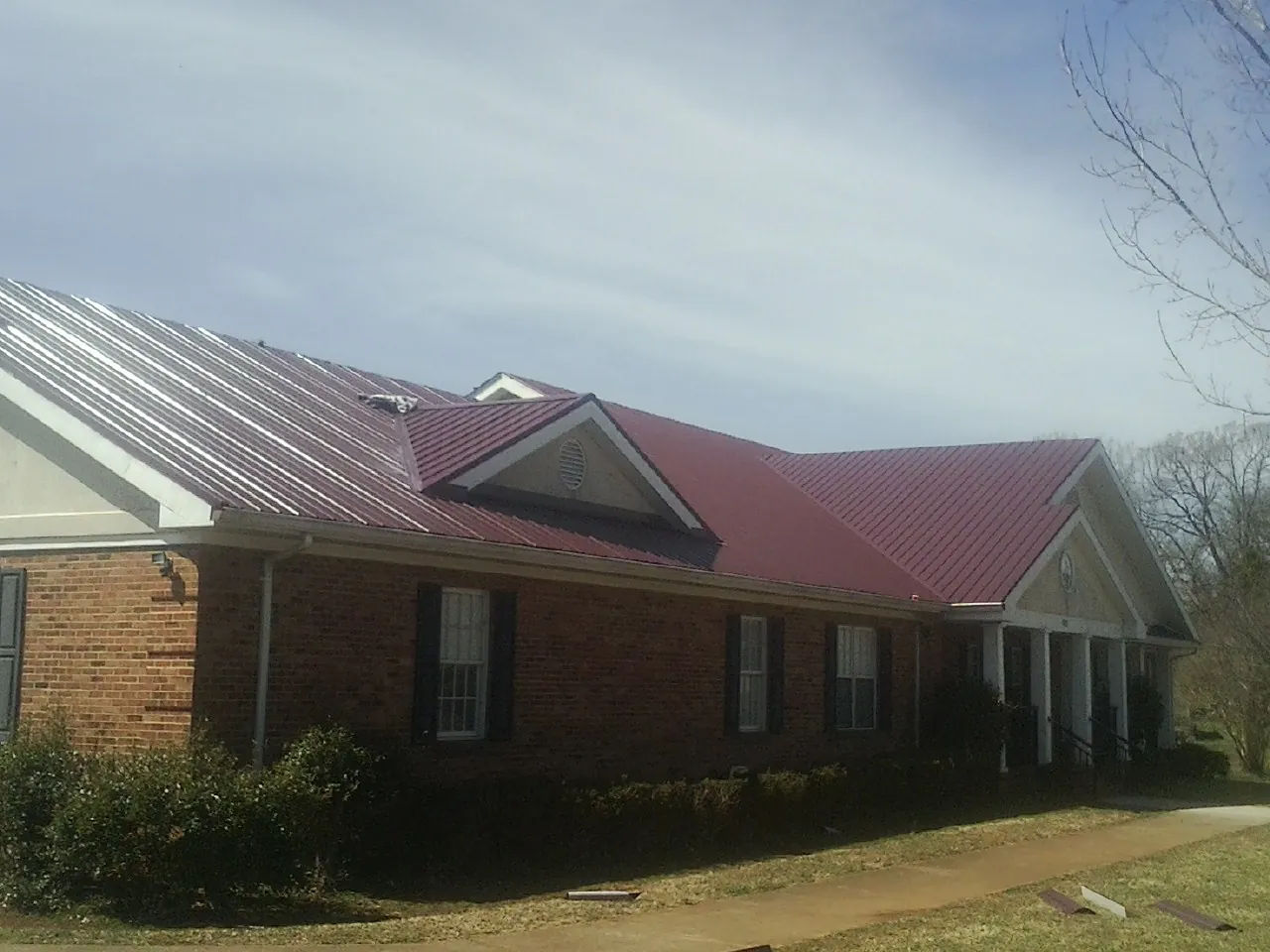 Red metal roof with gabled entries on a long brick building, from a Hail Damage Roof Repair job in Arley