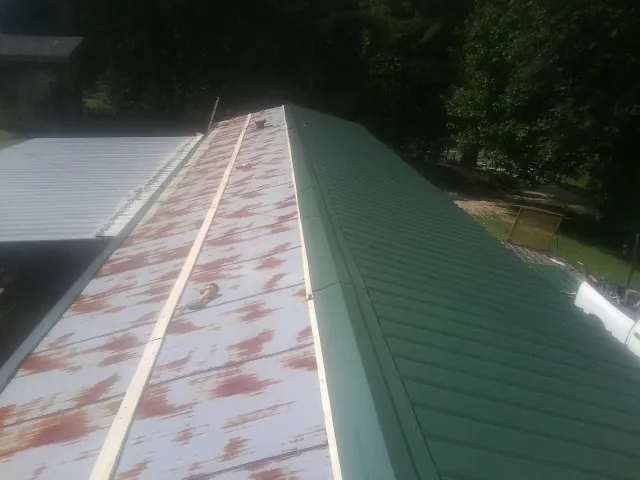 Old rusted panels beside newly installed green metal roofing — Wind Damage Roof Repair by Roofing Brothers in Arley