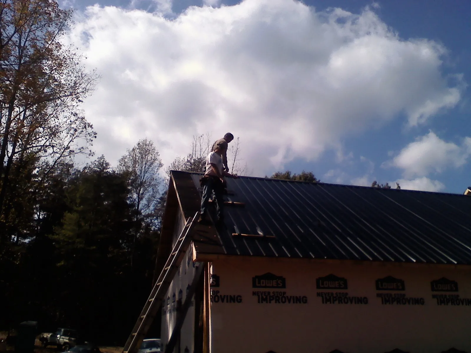 Roofer fastening dark metal panels high against a cloudy sky, from a Roof Inspection job in Arley