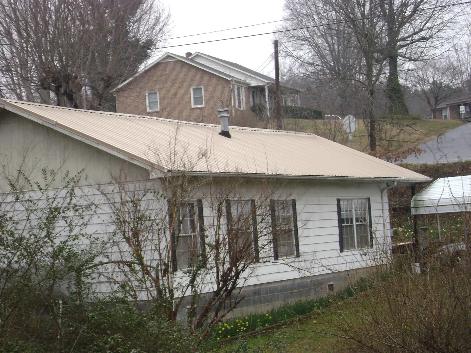 Tan metal roof on a white sided house set into a hillside — Commercial Roofing by Roofing Brothers in Arley