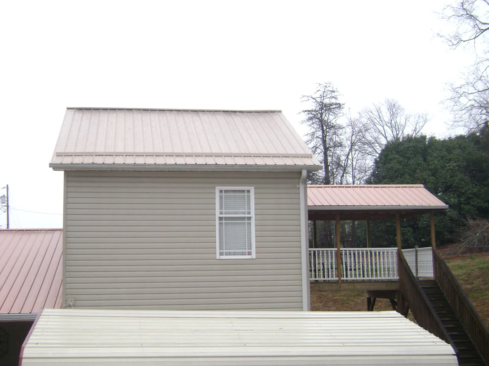 Tan metal roofs on a two story addition and attached porch, from a Roof Replacement job in Arley